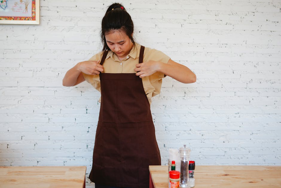 Asian woman wearing an apron in a small business restaurant with a brick wall background.