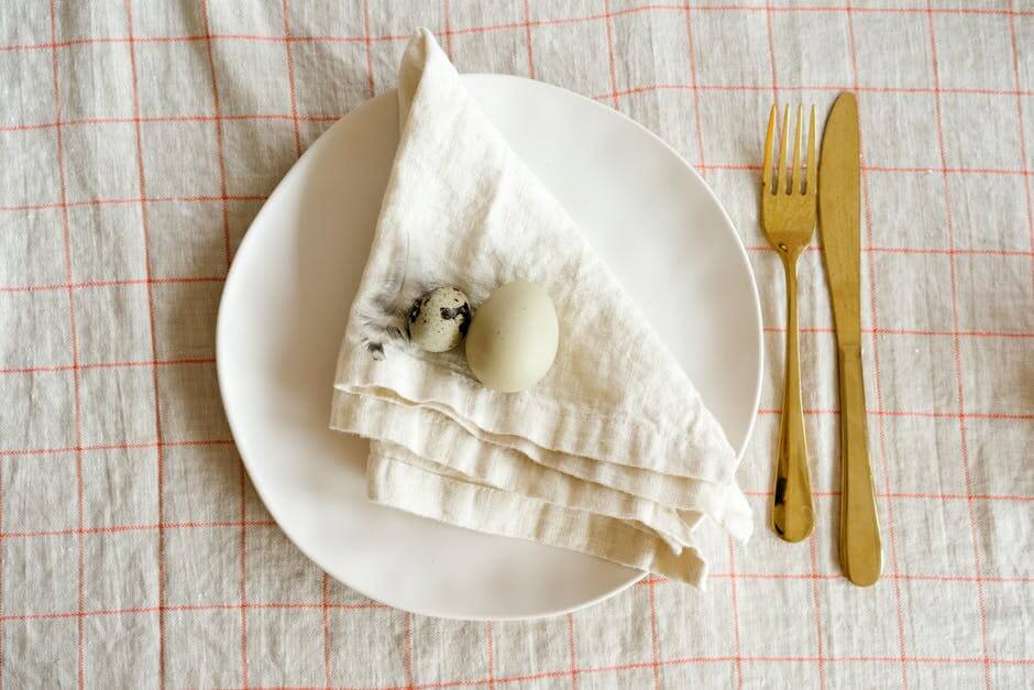 A minimalist table setting featuring quail eggs on a folded napkin with gold cutlery.