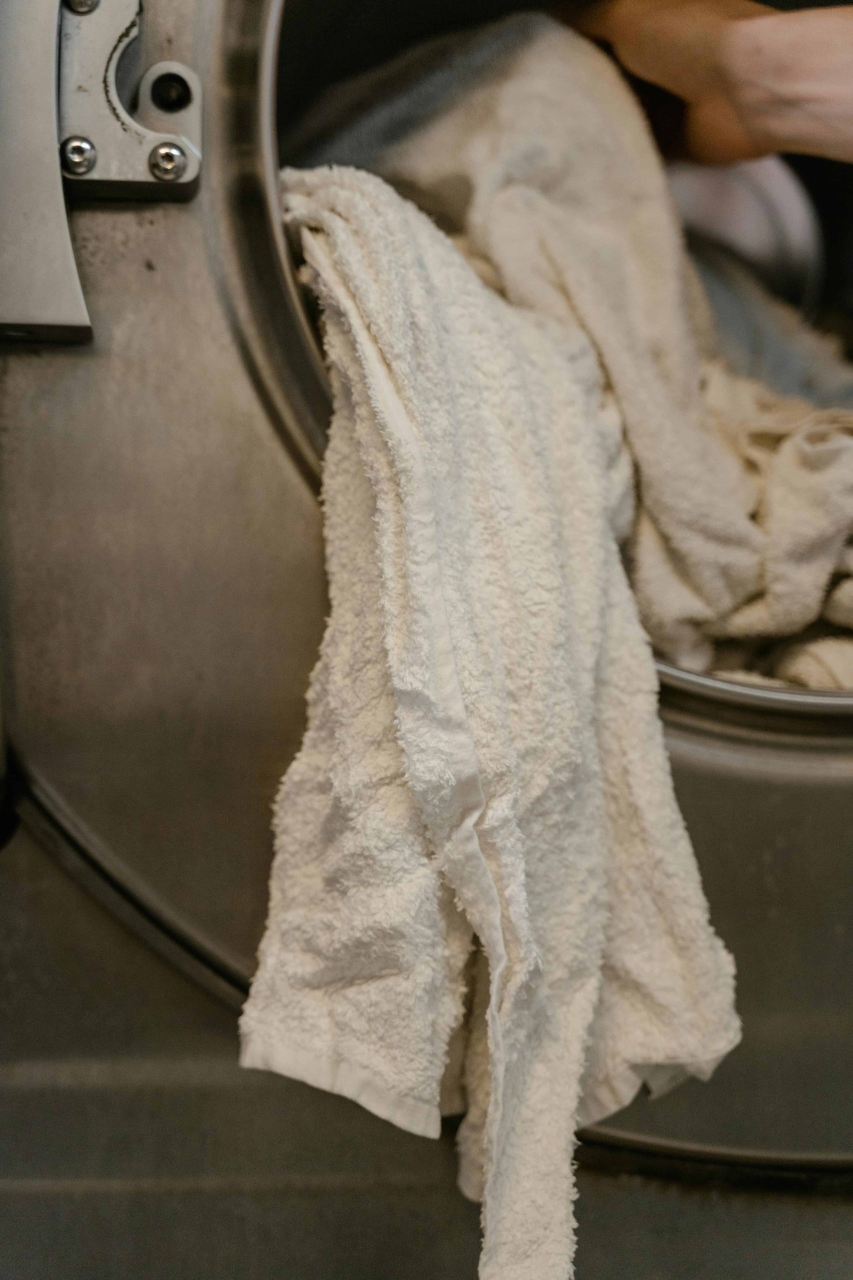 White towels partially hanging from a stainless steel washing machine.