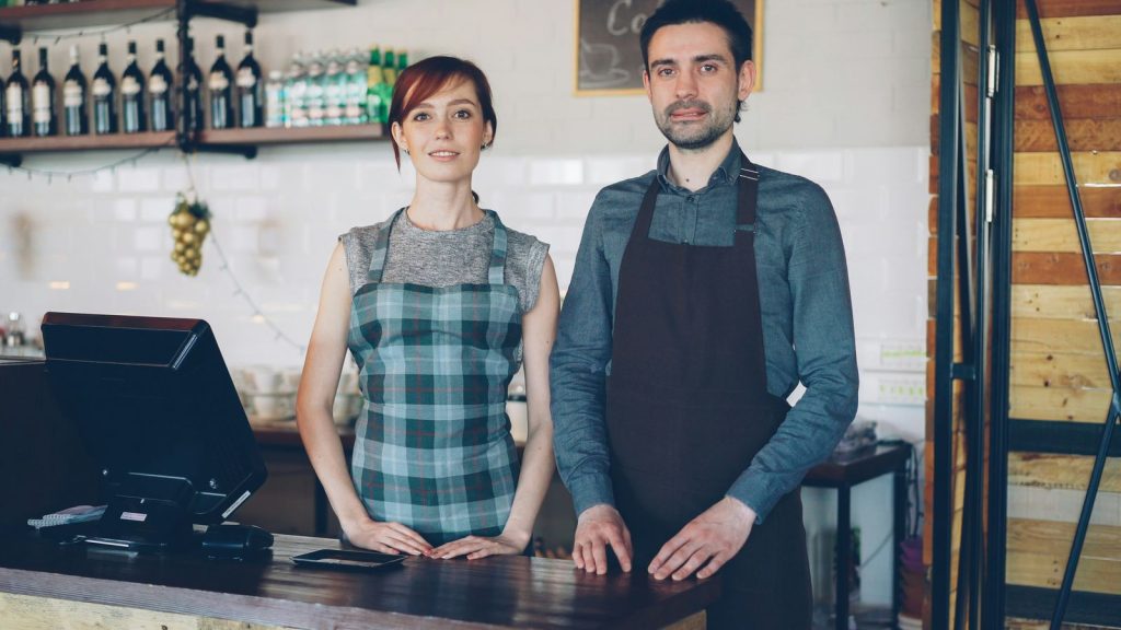 Two restaurant staff in aprons behind a counter